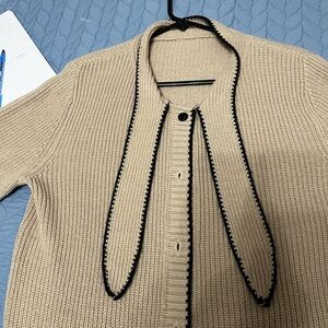 Elegant beige fine knit sweater with brown trim. Has tie neck and button front